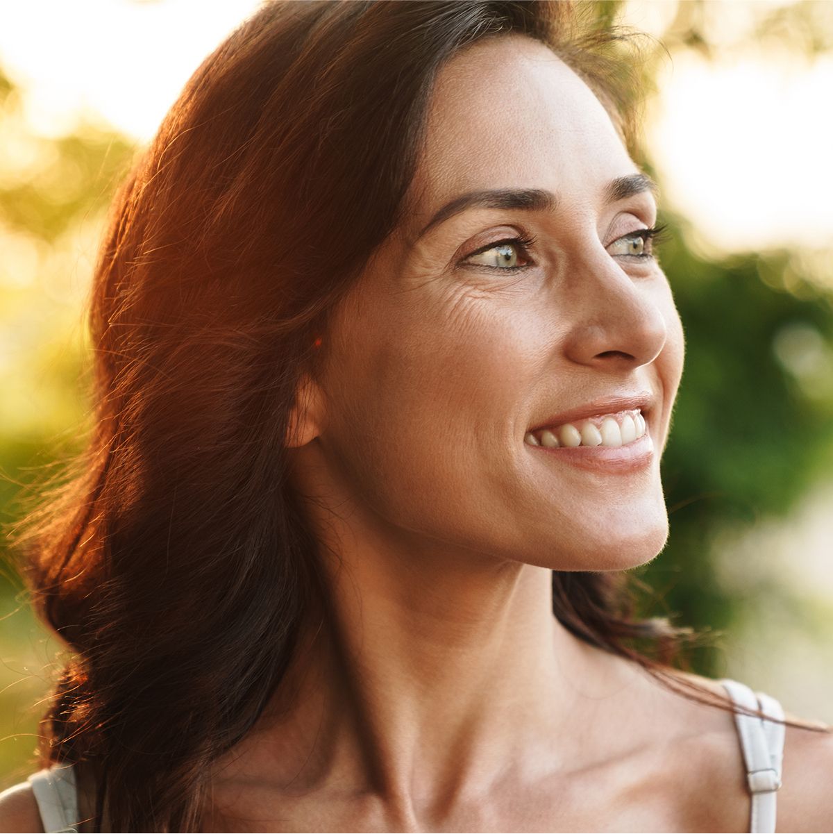 Smiling med spa patient model outdoors with natural sunlight background.