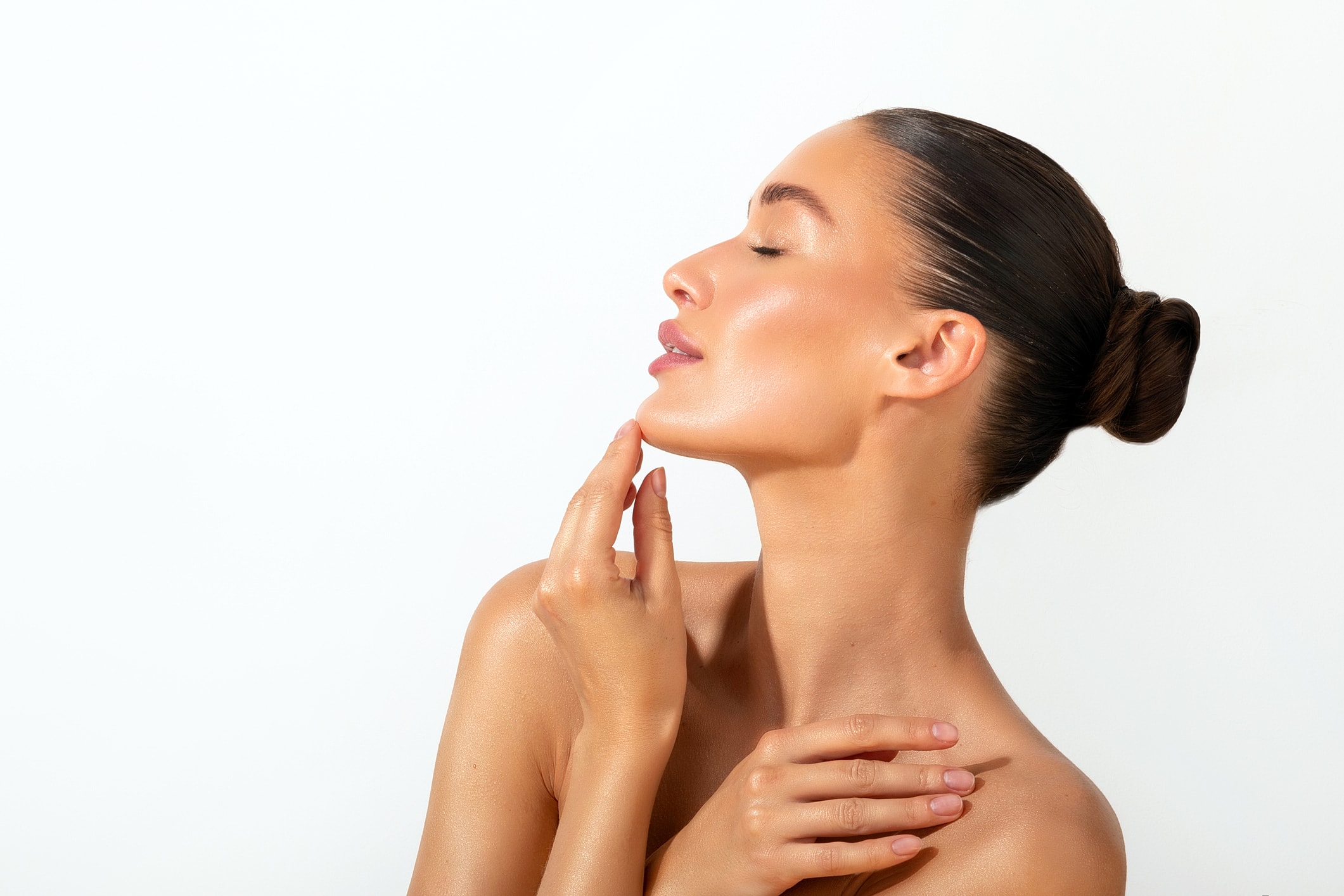 A woman with smooth, luminous skin tilts her chin upward, one hand resting at her collarbone.