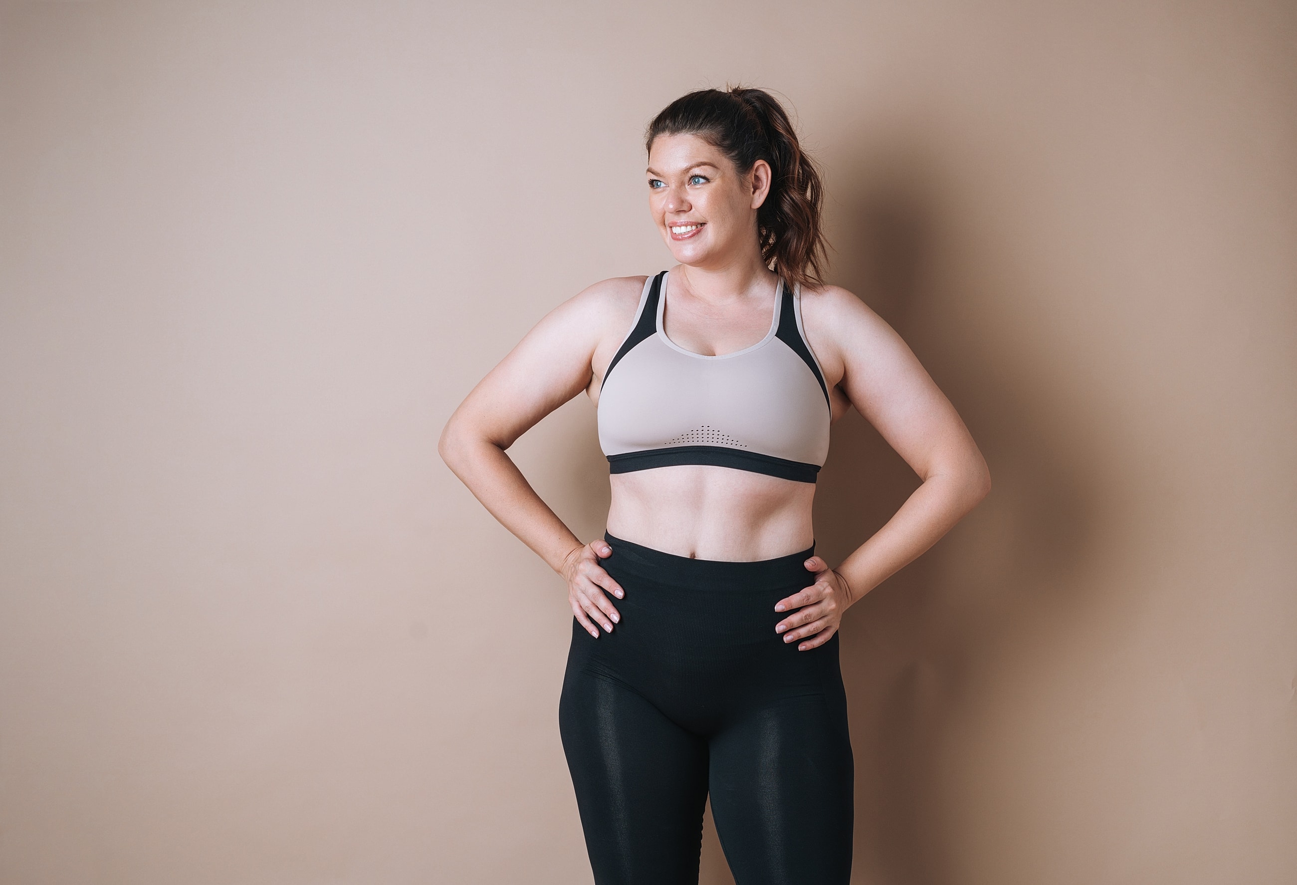 Smiling tirzepatide patient model in activewear against a neutral backdrop.